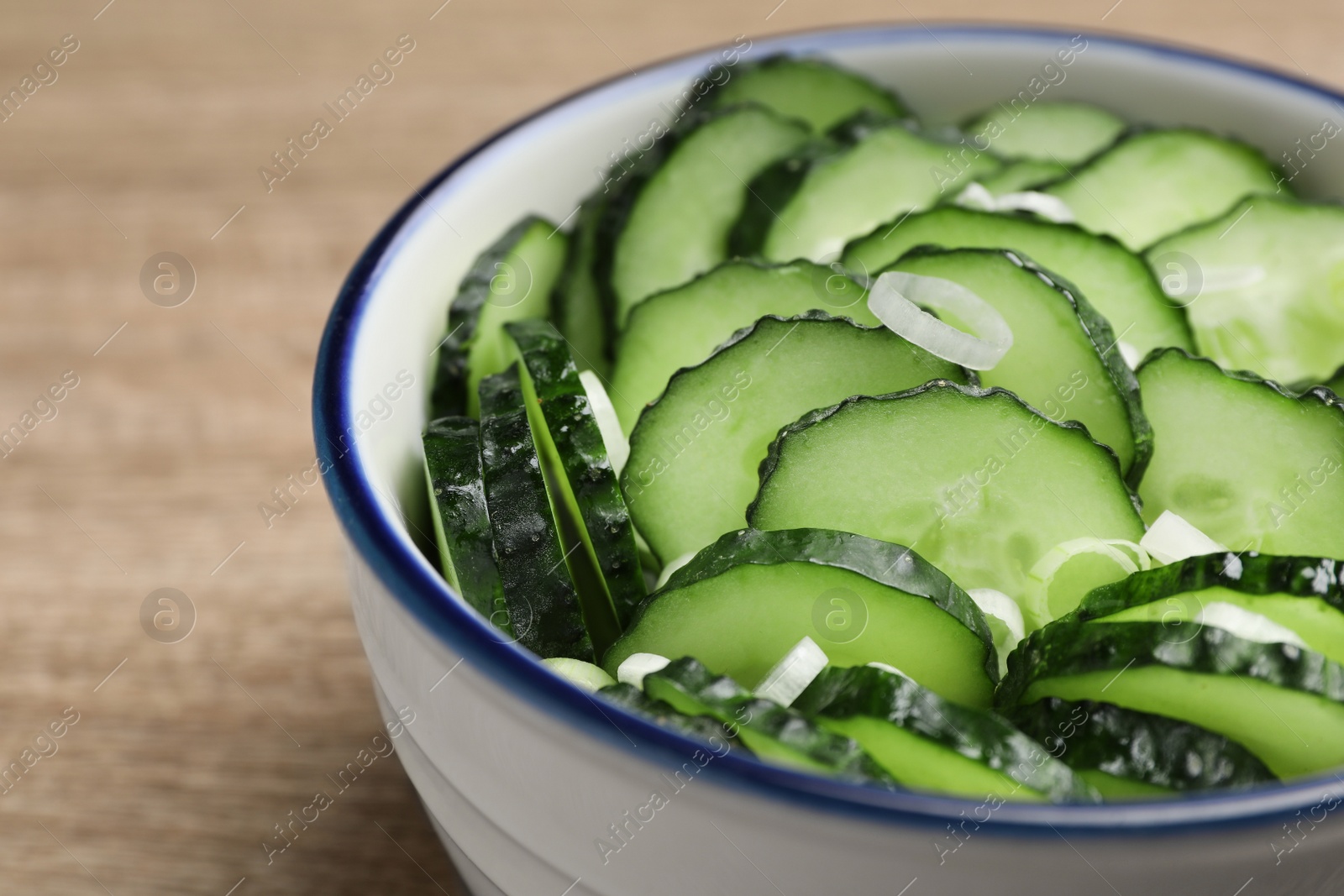 Photo of Delicious salad with cucumbers and green onion in bowl on wooden table, closeup