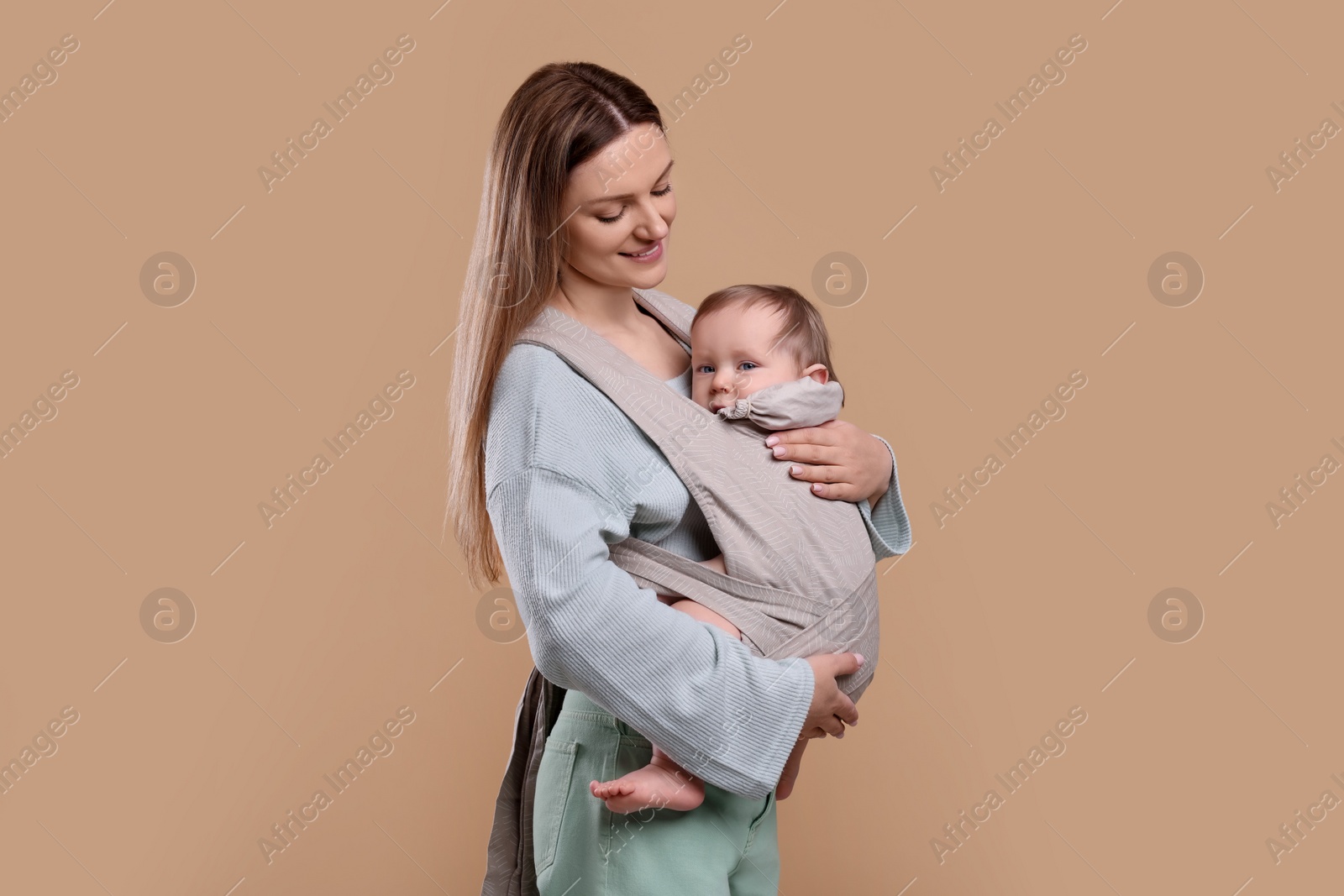 Photo of Mother holding her child in sling (baby carrier) on light brown background