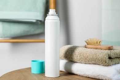 Photo of Bottle of dry shampoo, towels and hairbrush on wooden table indoors