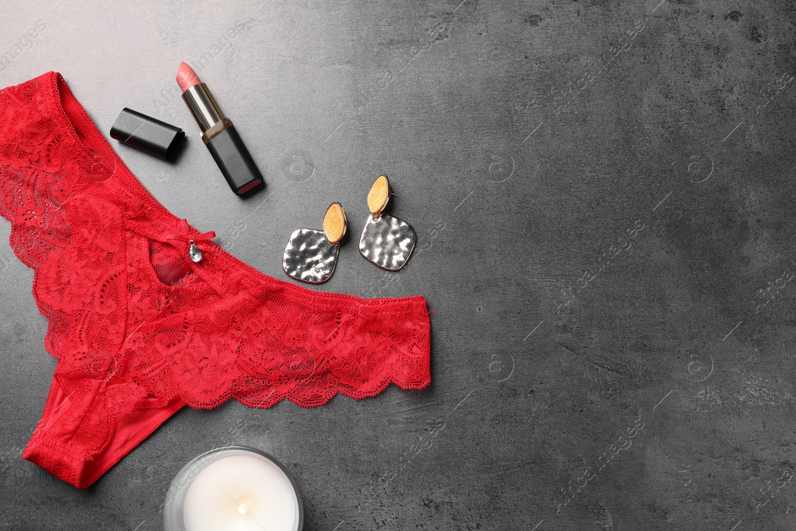 Photo of Flat lay composition with red women's underwear and burning candle on grey table. Space for text