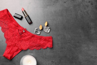 Photo of Flat lay composition with red women's underwear and burning candle on grey table. Space for text
