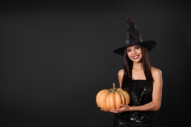 Beautiful woman wearing witch costume with pumpkin for Halloween party on black background, space for text