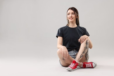 Photo of Smiling tattooed woman posing on grey background. Space for text