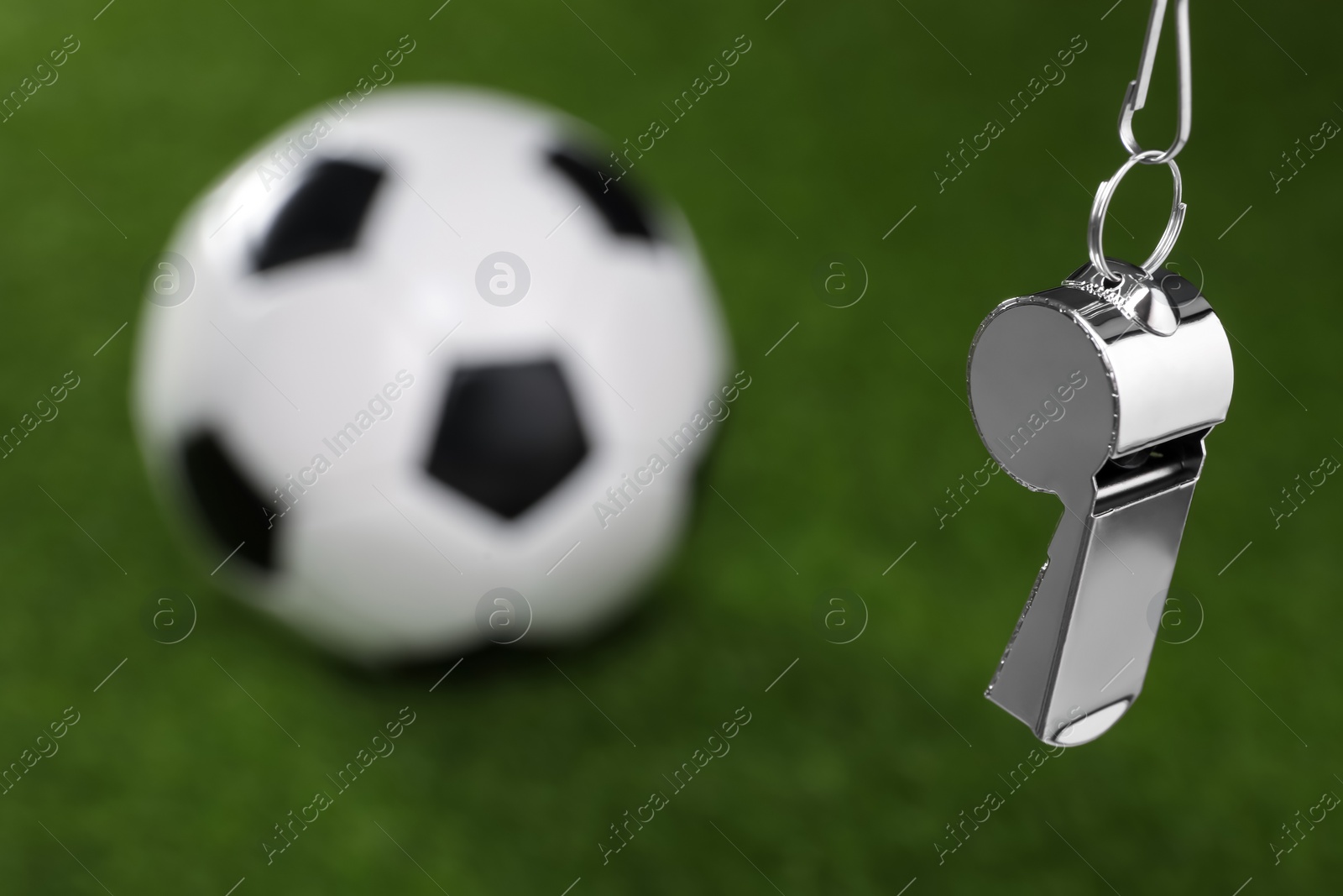 Photo of Football referee equipment. Metal whistle and soccer ball on green grass, closeup with space for text