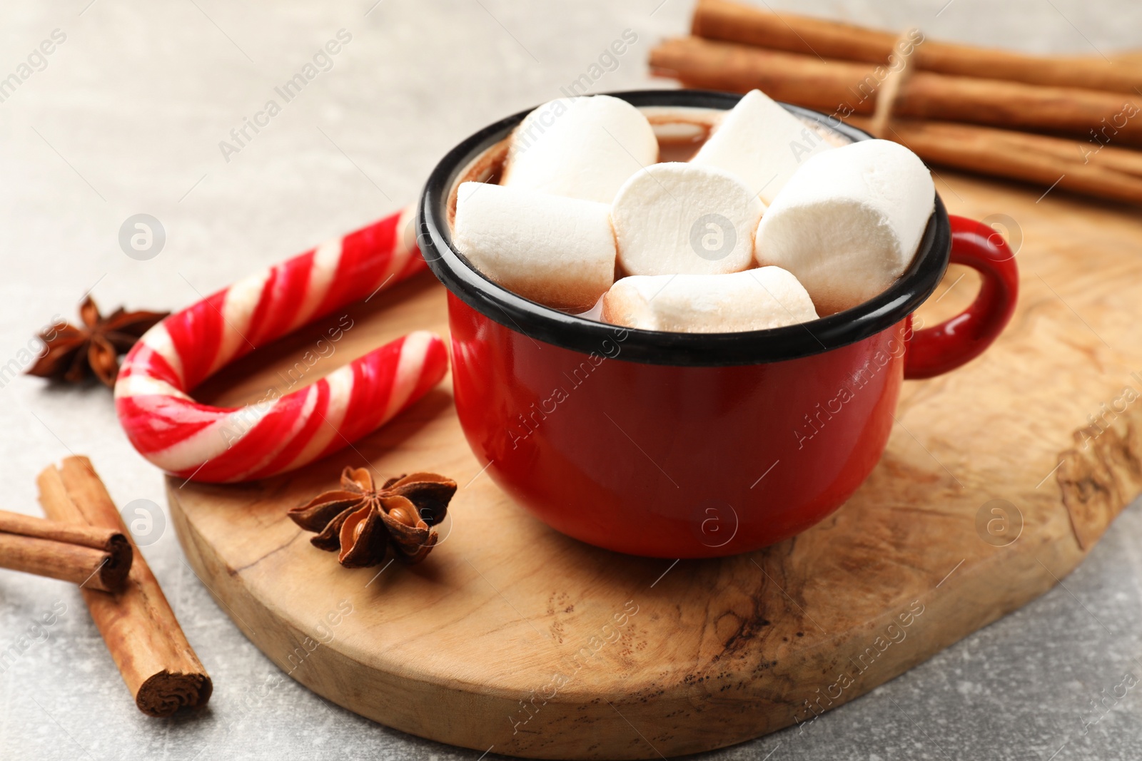 Photo of Tasty hot chocolate with marshmallows, candy cane and spices on light grey table, closeup