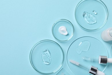 Photo of Petri dishes with samples of cosmetic serums, bottle and pipettes on light blue background, flat lay. Space for text