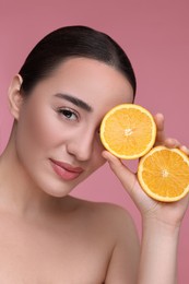 Beautiful young woman with pieces of orange on pink background