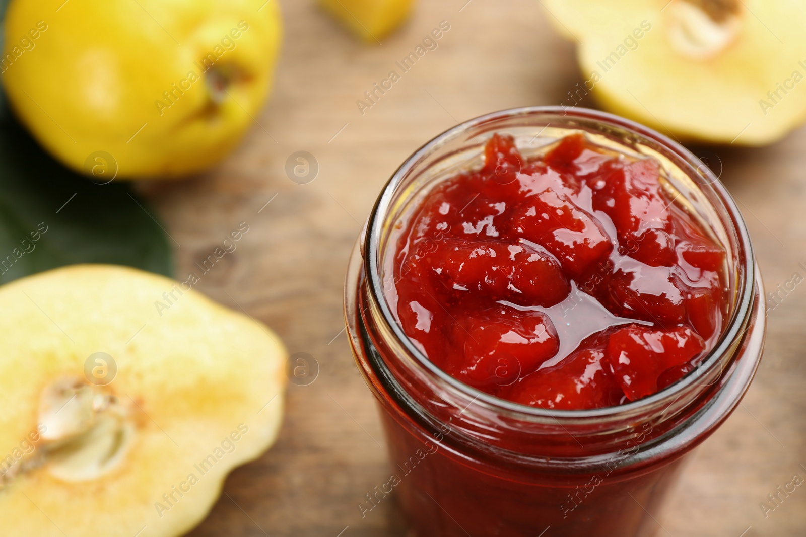 Photo of Delicious quince jam and fruits on wooden table, closeup