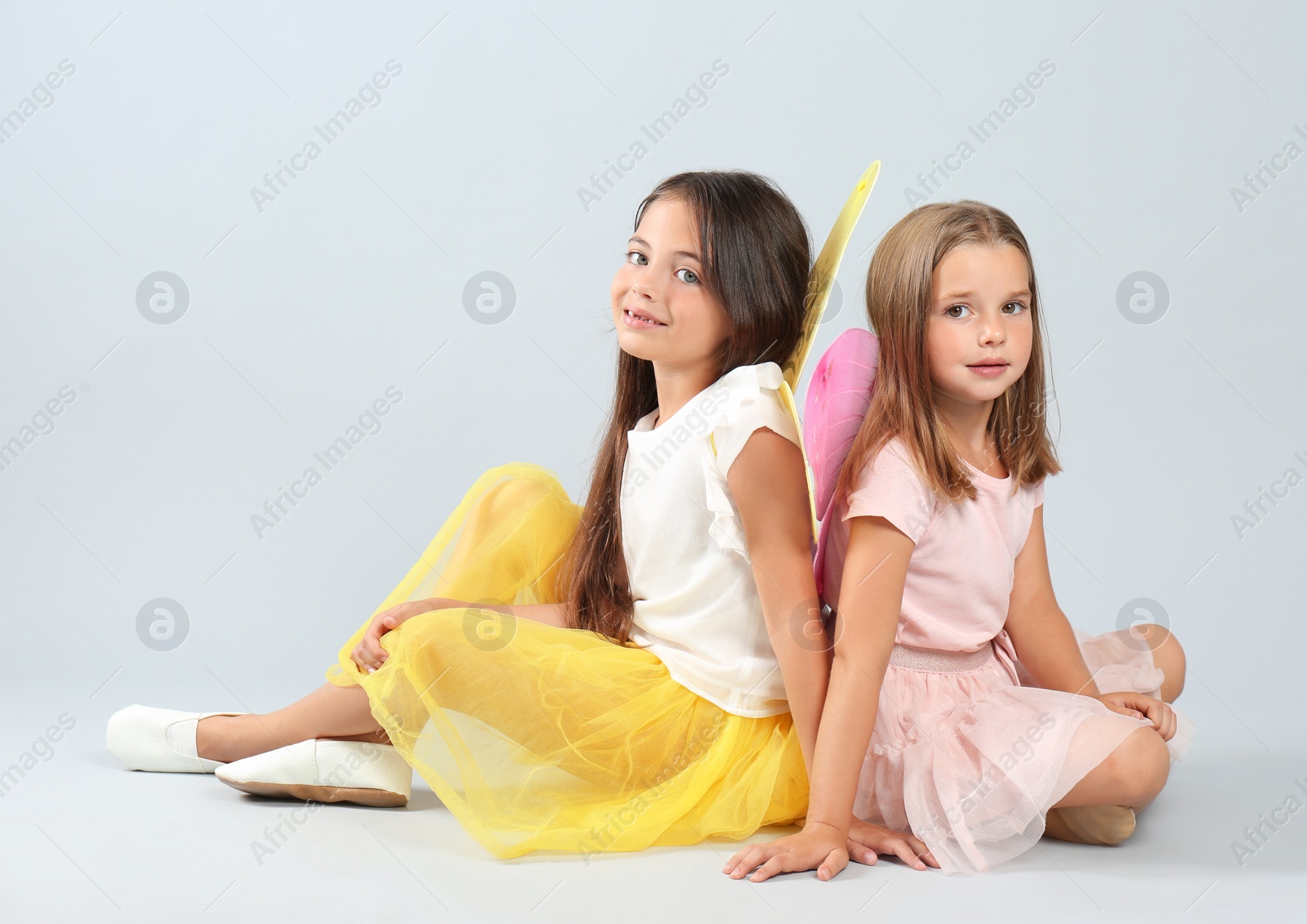 Photo of Cute little girls in fairy costumes with wings on light background