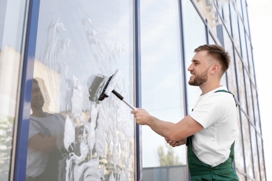 Male cleaner wiping window glass with squeegee from outside