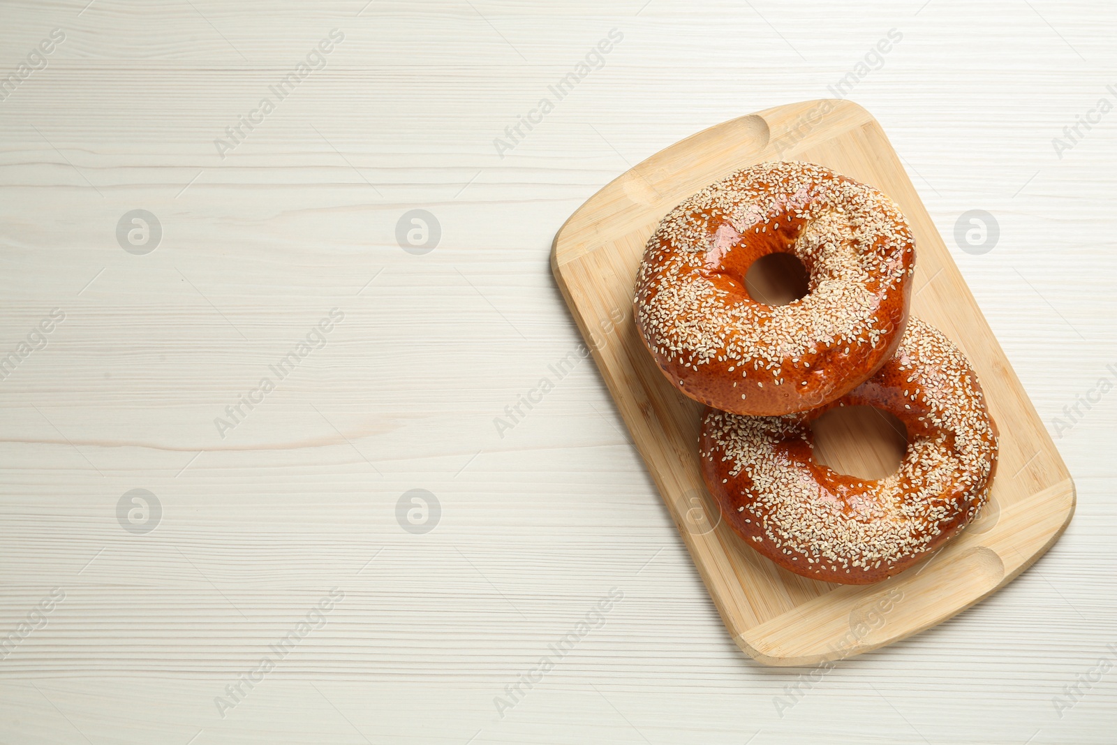 Photo of Delicious fresh bagels with sesame seeds on white wooden table, top view. Space for text