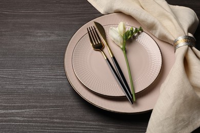 Stylish table setting. Plates, cutlery, napkin and floral decor on dark wooden background, space for text