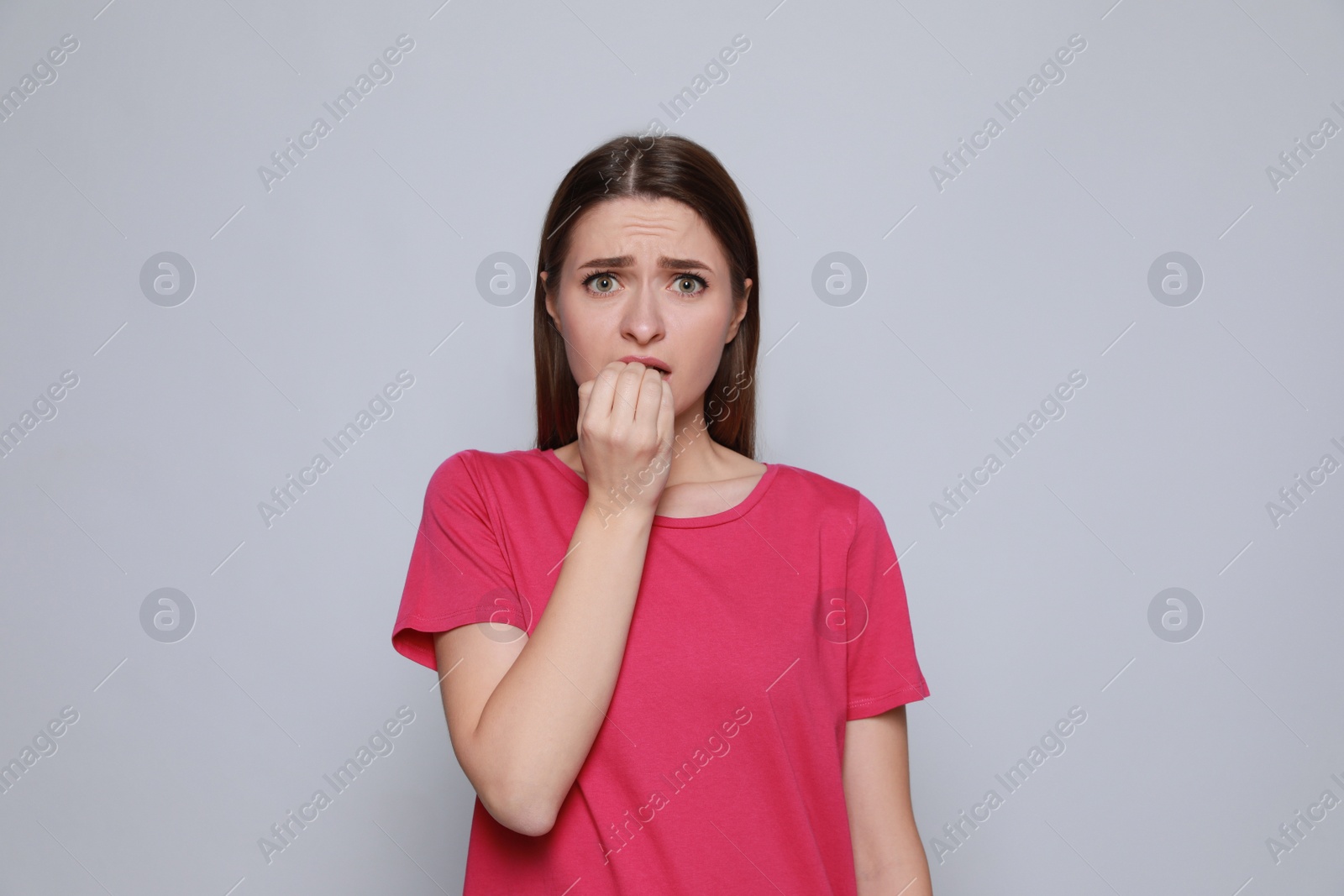 Photo of Young woman biting her nails on light grey background