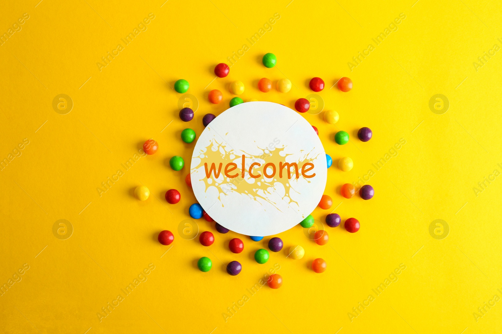 Image of Colorful candies and card with word WELCOME on yellow background, flat lay