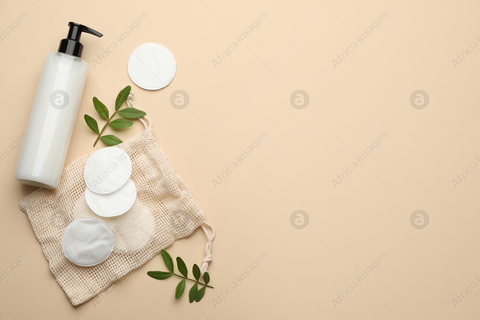 Photo of Cotton pads, leaves and makeup removal product on beige background, flat lay. Space for text