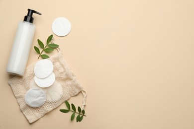 Photo of Cotton pads, leaves and makeup removal product on beige background, flat lay. Space for text