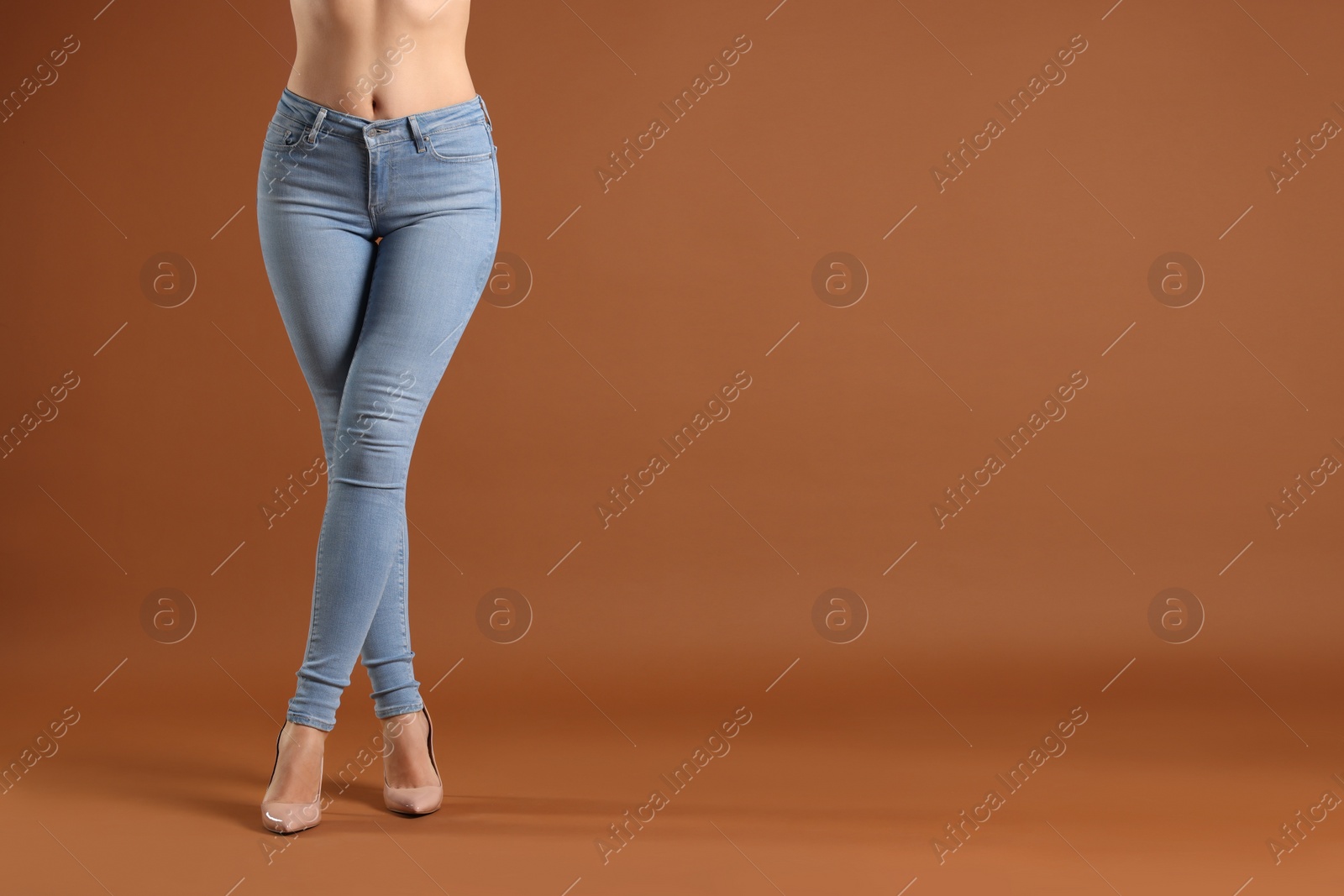 Photo of Woman wearing stylish light blue jeans and high heels shoes on brown background, closeup. Space for text