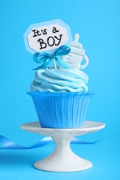 Beautifully decorated baby shower cupcake with cream and boy topper on light blue background