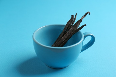 Cup with vanilla sticks on blue background