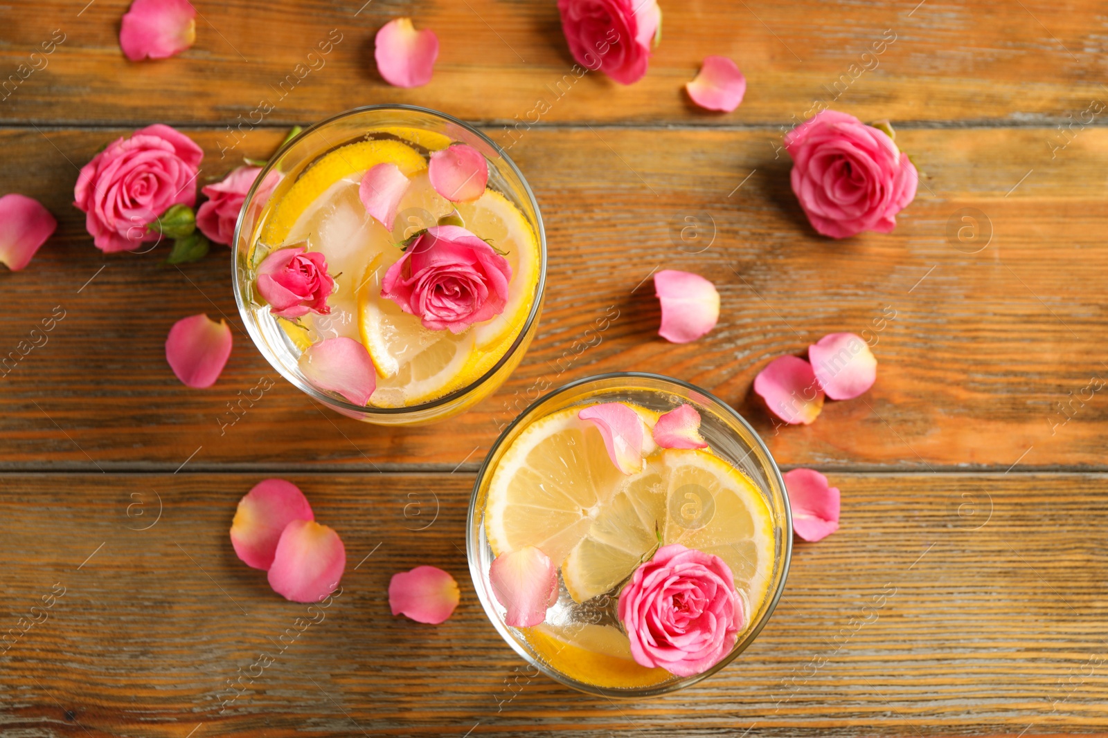 Photo of Tasty refreshing lemon drink with roses on wooden table, flat lay