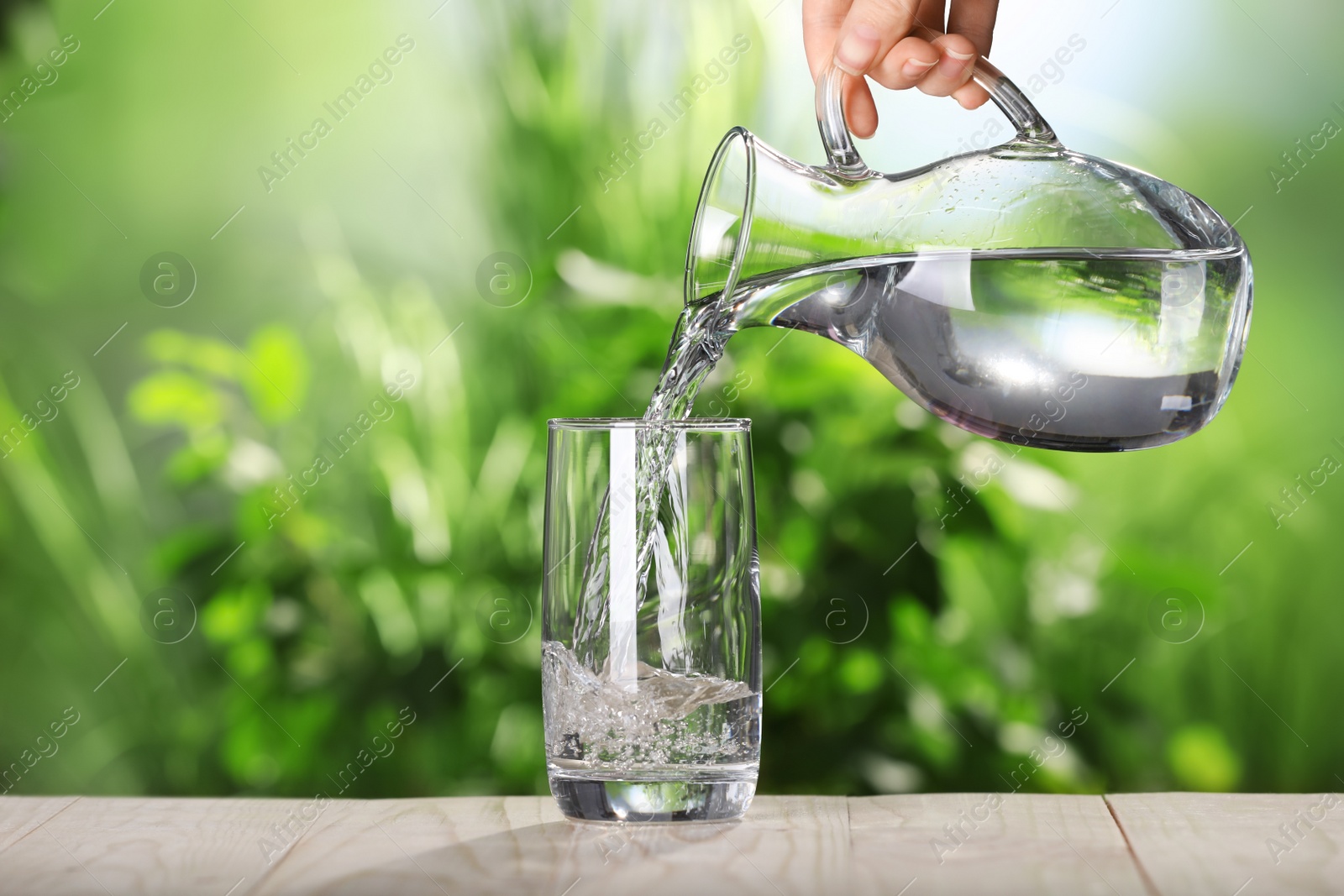 Photo of Woman pouring water from jug into glass on grey wooden table outdoors, closeup