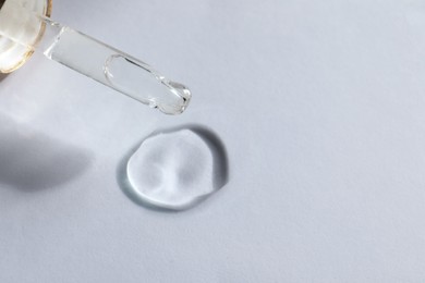 Photo of Dripping cosmetic oil from pipette onto white background, closeup. Space for text