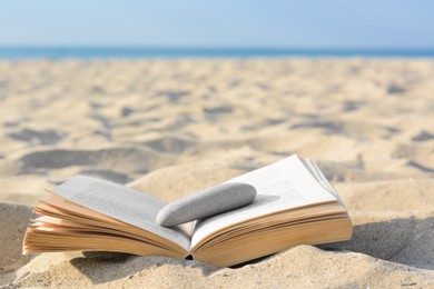 Open book with stone on sandy beach near sea, space for text