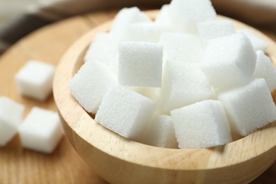 Photo of White sugar cubes in bowl on wooden board, closeup