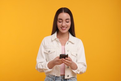 Photo of Happy young woman using smartphone on yellow background