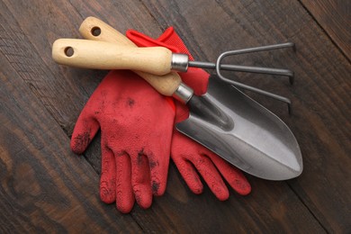 Gardening gloves, trowel and rake on wooden table, top view