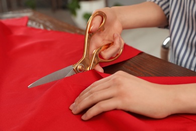 Photo of Woman cutting fabric with sharp scissors at wooden table indoors, closeup