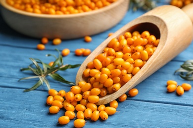 Photo of Ripe sea buckthorn berries on blue wooden table, closeup