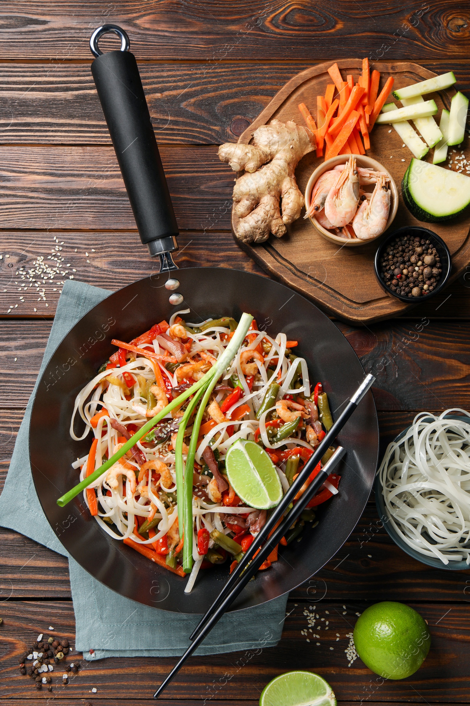Photo of Shrimp stir fry with noodles and vegetables in wok on wooden table, flat lay