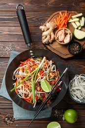 Shrimp stir fry with noodles and vegetables in wok on wooden table, flat lay