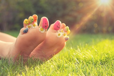 Photo of Teenage girl with drawn smiling faces and chamomiles between toes outdoors, closeup. Space for text