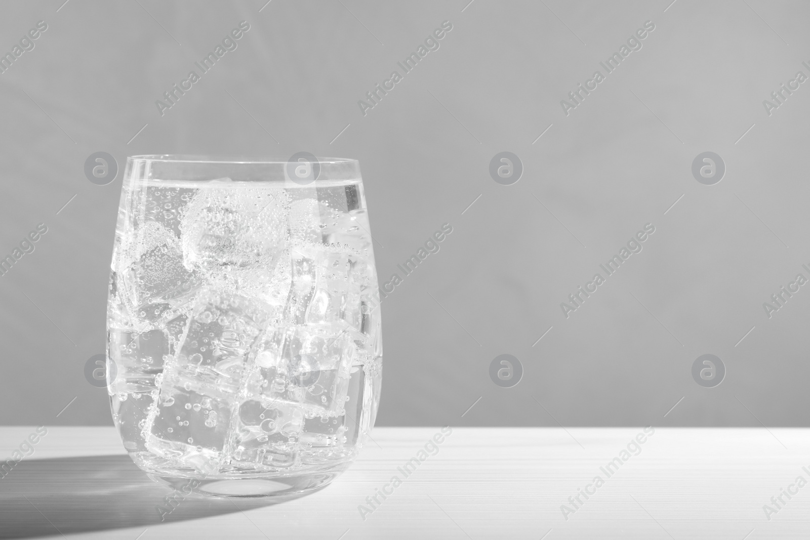 Photo of Glass of soda water with ice on white wooden table. Space for text