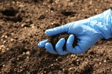 Scientist holding pile of soil above ground, closeup. Space for text