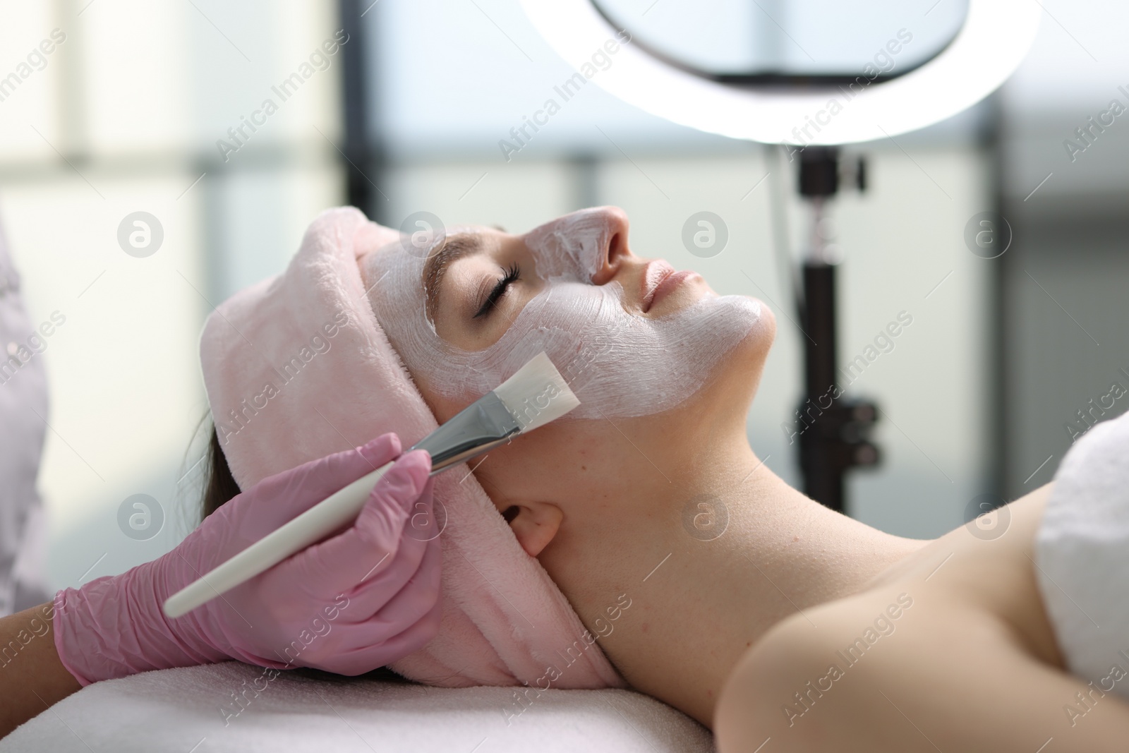 Photo of Cosmetologist applying mask on woman's face in clinic, closeup