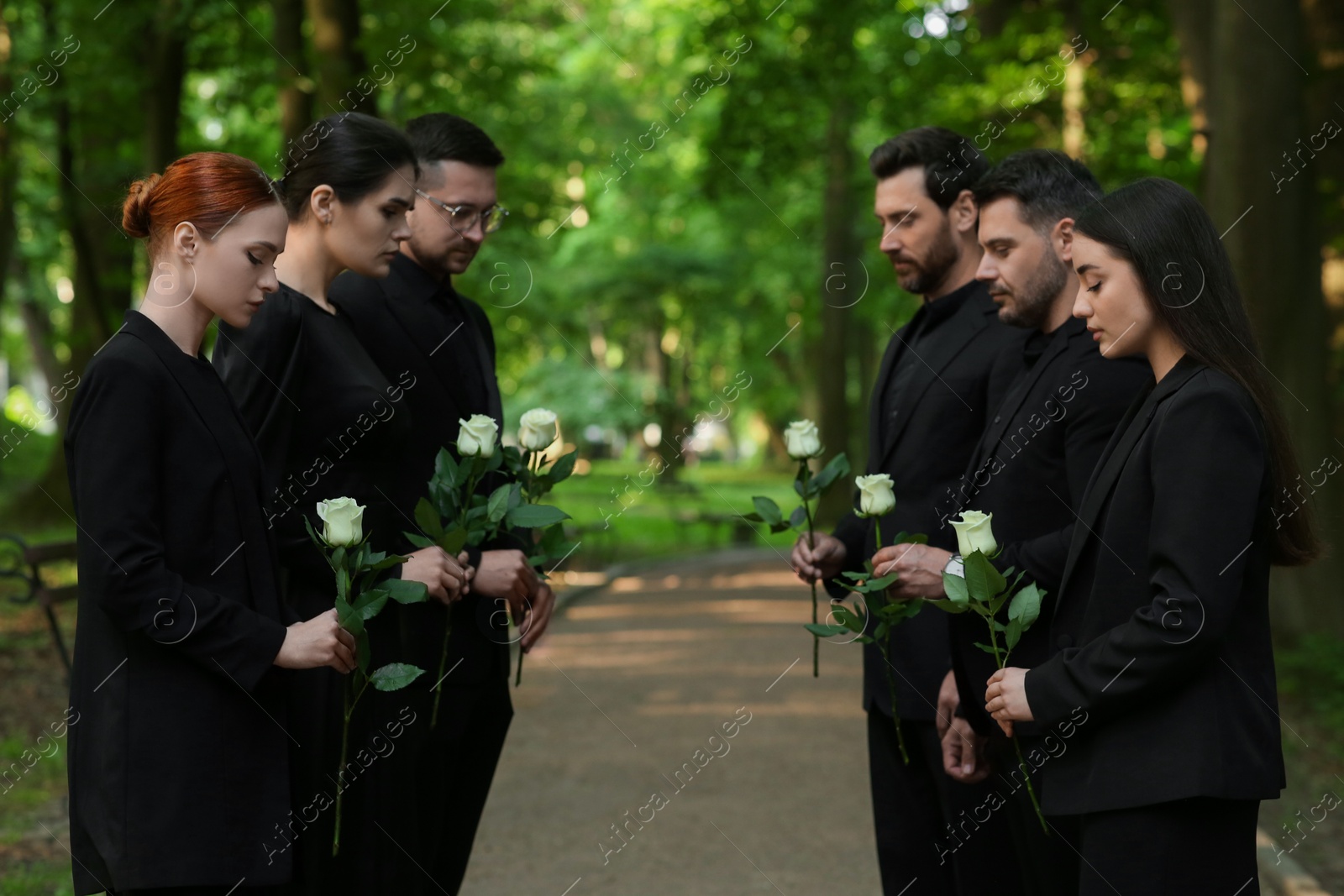 Photo of Funeral ceremony. Sad people with white rose flowers mourning outdoors