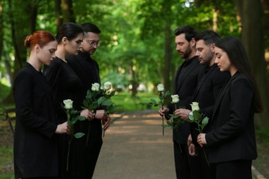 Photo of Funeral ceremony. Sad people with white rose flowers mourning outdoors