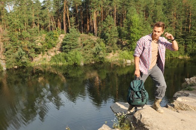 Young man on rock near lake and forest. Camping season