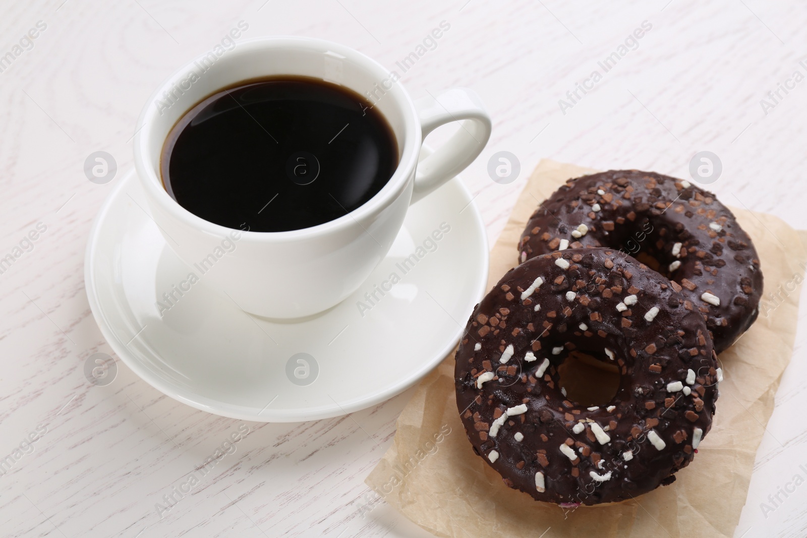 Photo of Two delicious fresh donuts with sprinkles and cup of coffee on white wooden table