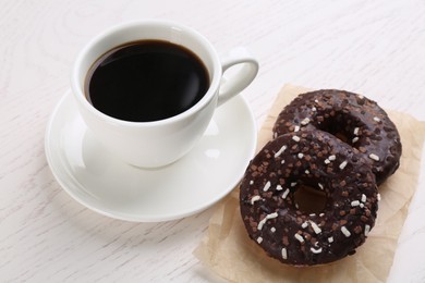 Photo of Two delicious fresh donuts with sprinkles and cup of coffee on white wooden table