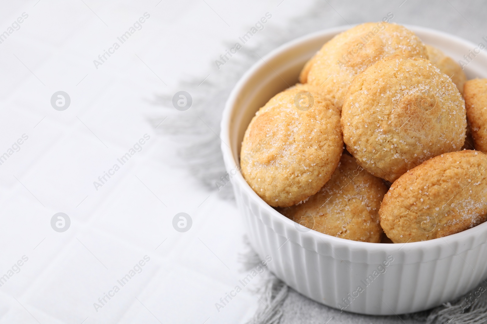 Photo of Tasty sugar cookies in bowl on white tiled table, closeup. Space for text