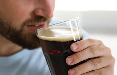 Young man with cold kvass indoors, closeup. Traditional Russian summer drink