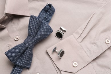 Stylish blue bow tie and cufflinks on beige shirt, top view