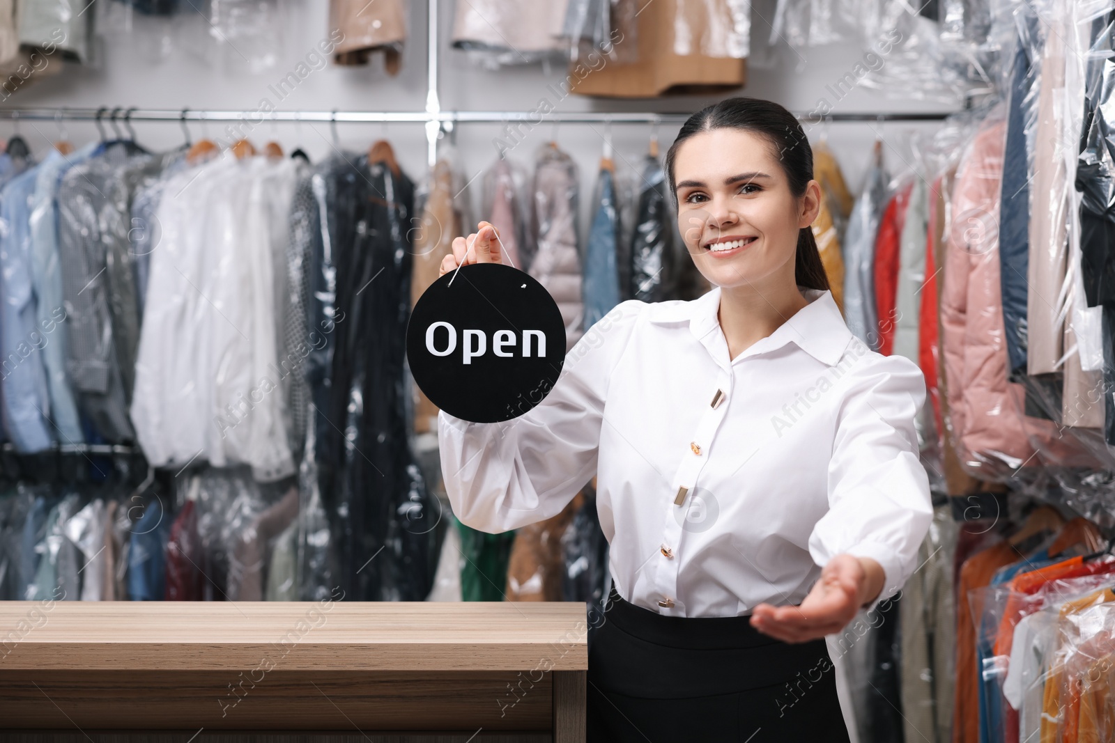 Photo of Dry-cleaning service. Happy worker holding Open sign indoors, space for text