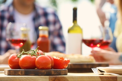 Photo of Wooden board with tomatoes on table outdoors. Summer picnic