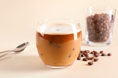 Photo of Refreshing iced coffee with milk in glass and beans on beige background
