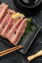 Photo of Pieces of delicious tuna steak served on black table, flat lay